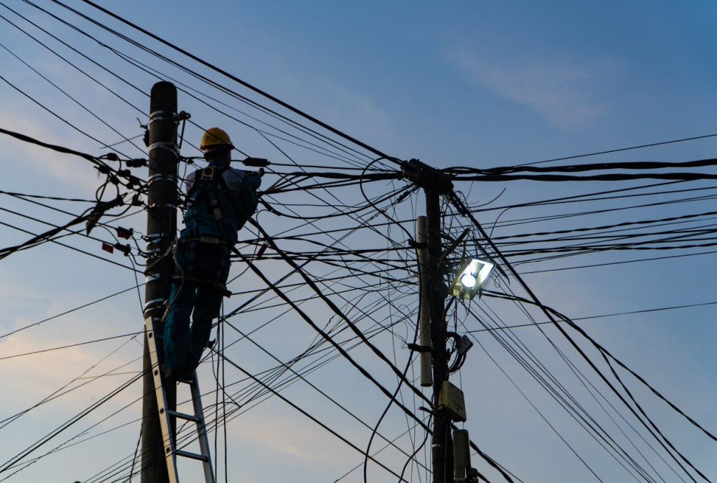 Silhouette of an electrician fixing power lines at sunset in Ubud, Bali.